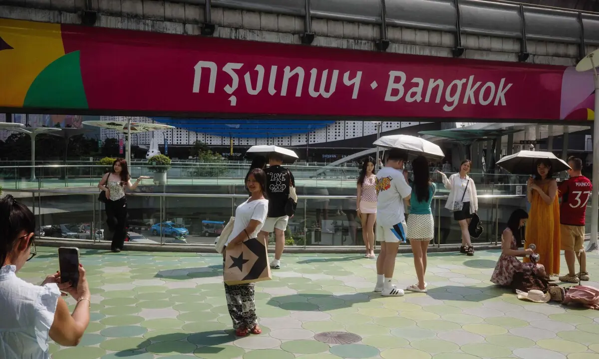 People use umbrellas as they pose for photos at the Pathumwan Intersection Skywalk in Bangkok on April 29, 2026.
